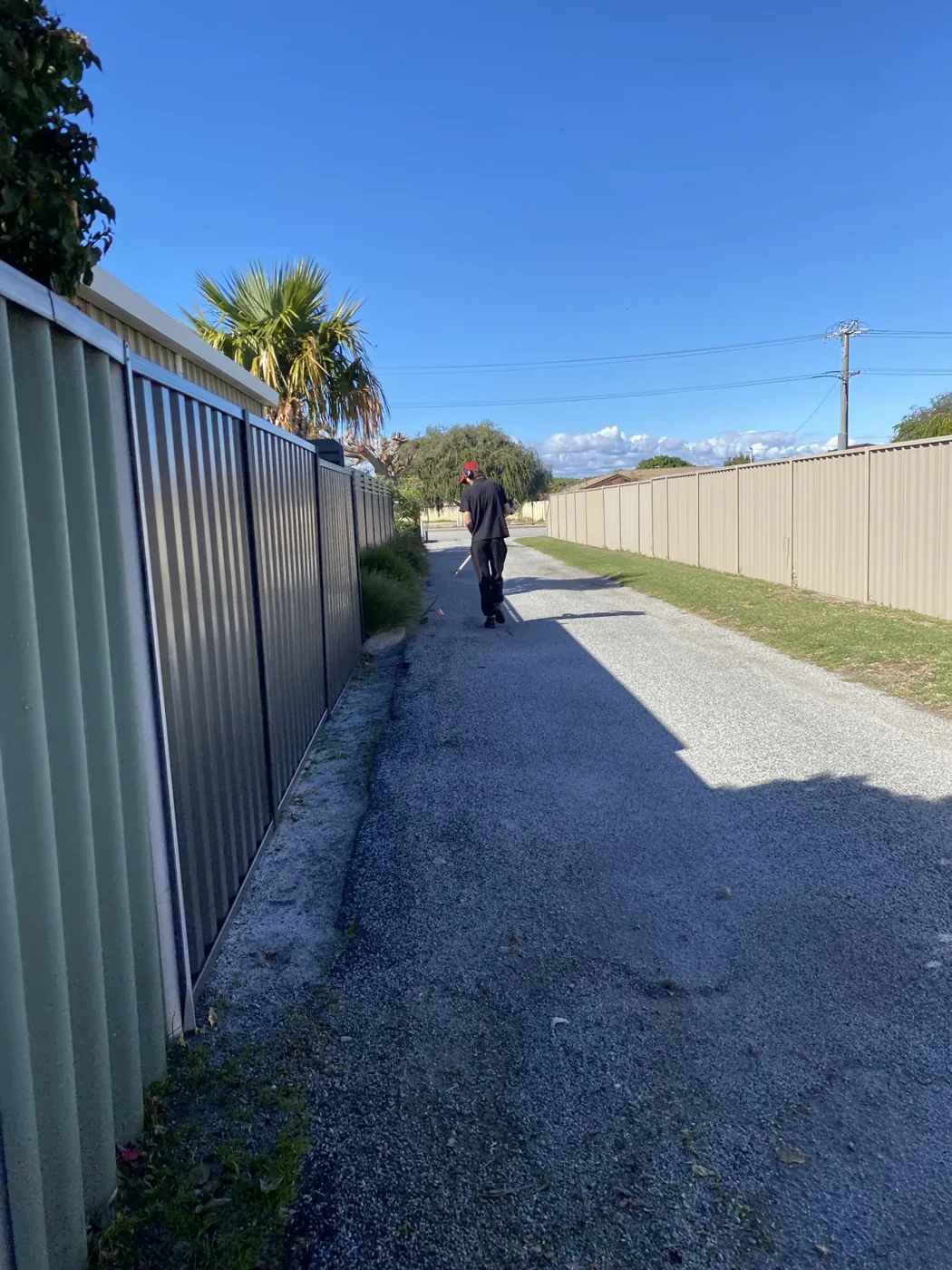 Lawn maintenance along a fenced access lane, with a worker on the path